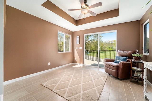 9703 Tower Rd, South Lyon, MI 48178 - living area featuring a tray ceiling, baseboards, a ceiling fan, and light wood-style flooring
