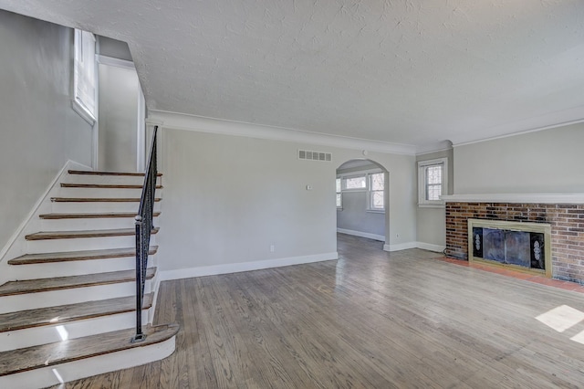 18613 Santa Rosa Dr, Detroit, MI 48221 - unfurnished living room featuring arched walkways, a textured ceiling, wood finished floors, ornamental molding, and a fireplace