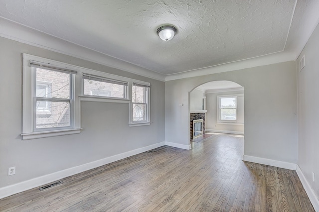 18613 Santa Rosa Dr, Detroit, MI 48221 - unfurnished room featuring arched walkways, a textured ceiling, wood finished floors, a brick fireplace, and baseboards
