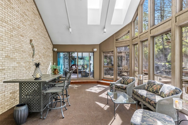 sunroom featuring high vaulted ceiling, carpet floors, a skylight, brick wall, and plenty of natural light