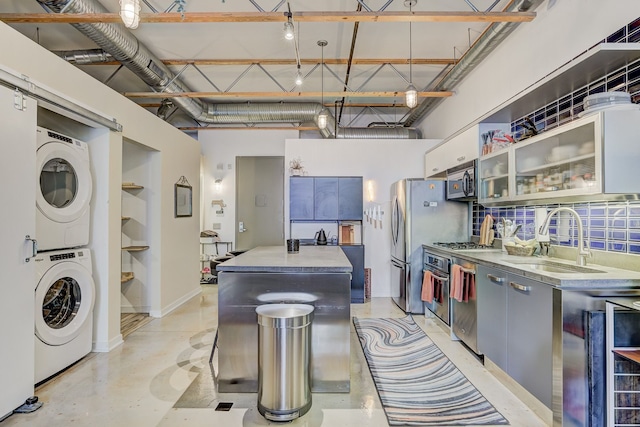 111 N Main St Unit 209, Royal Oak, MI 48067 - kitchen featuring stacked washer / drying machine, a sink, appliances with stainless steel finishes, a center island, and glass insert cabinets