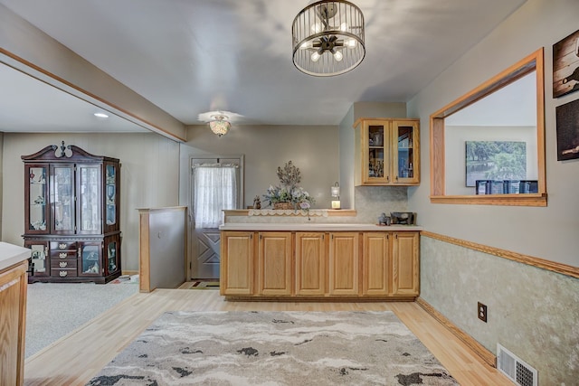 kitchen featuring light wood finished floors, light countertops, glass insert cabinets, a peninsula, and a chandelier