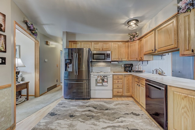 kitchen with appliances with stainless steel finishes, light countertops, a sink, tasteful backsplash, and light wood finished floors