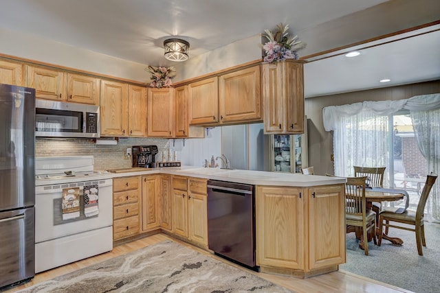 kitchen with stainless steel appliances, a peninsula, light countertops, backsplash, and a sink