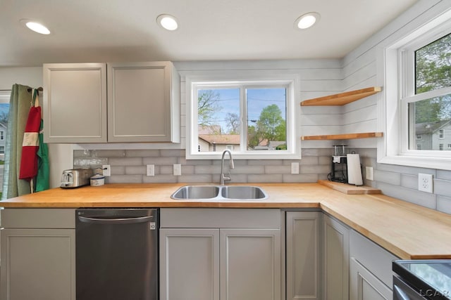 kitchen with stainless steel dishwasher, a sink, wood counters, backsplash, and gray cabinetry