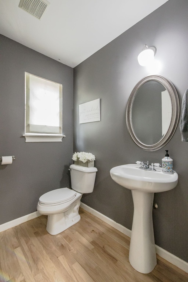 half bath featuring wood finished floors, toilet, baseboards, and a sink
