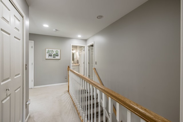 hall with an upstairs landing, light colored carpet, recessed lighting, and baseboards