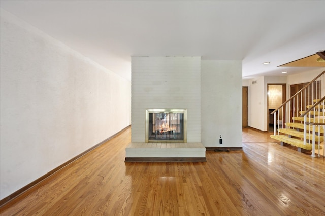 unfurnished living room with wood finished floors, stairs, a brick fireplace, and baseboards
