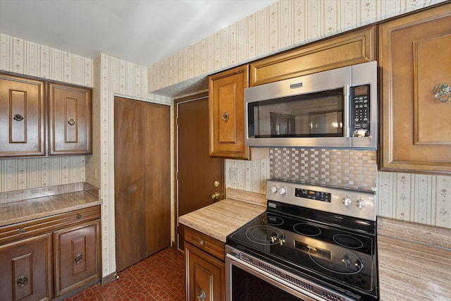 kitchen featuring appliances with stainless steel finishes, wallpapered walls, light countertops, and brown cabinetry