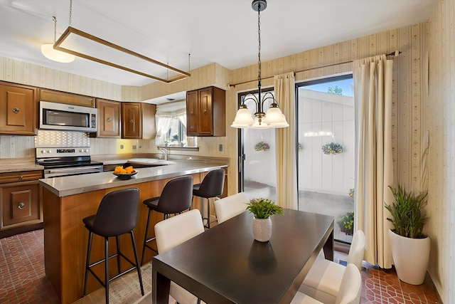 kitchen with stainless steel appliances, wallpapered walls, a breakfast bar, pendant lighting, and brick patterned floors
