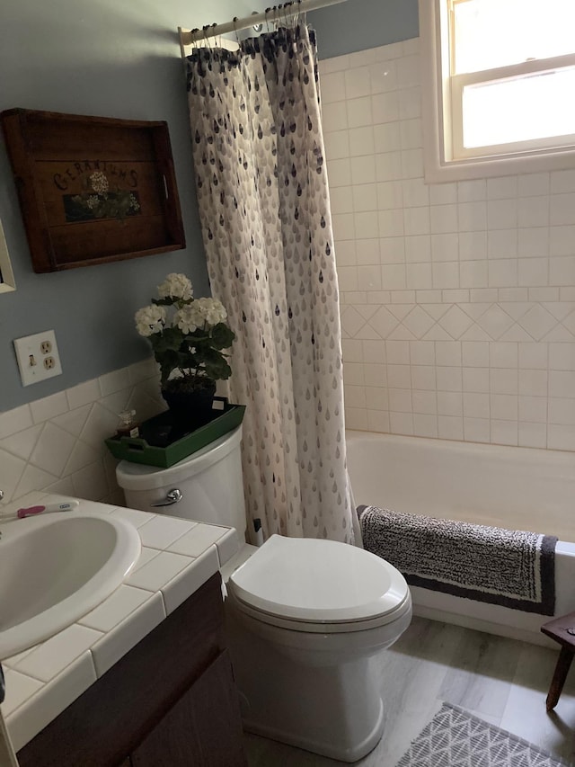 bathroom with toilet, shower / bath combination with curtain, vanity, and tile walls