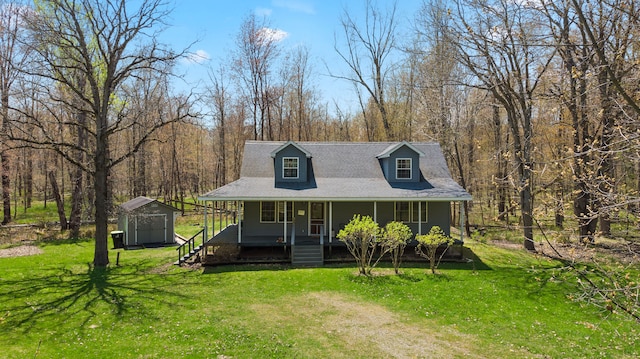 view of front of home featuring covered porch, a storage shed, an outdoor structure, a front lawn, and a wooded view