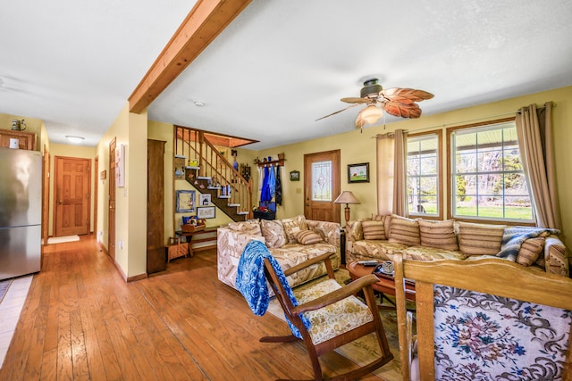 living room featuring stairs, a ceiling fan, light wood-style floors, and beamed ceiling