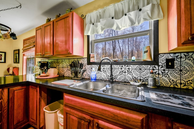 kitchen featuring a sink, tasteful backsplash, dark countertops, reddish brown cabinets, and a peninsula
