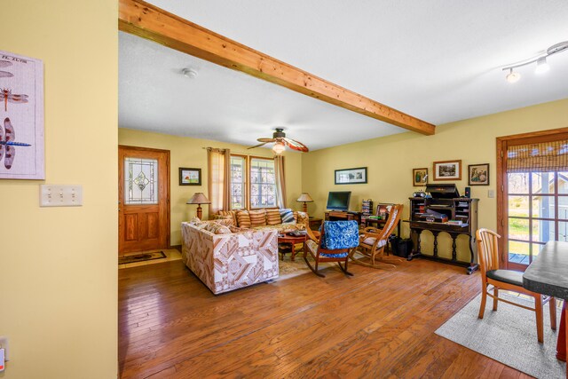 living area with beam ceiling, wood-type flooring, and a ceiling fan