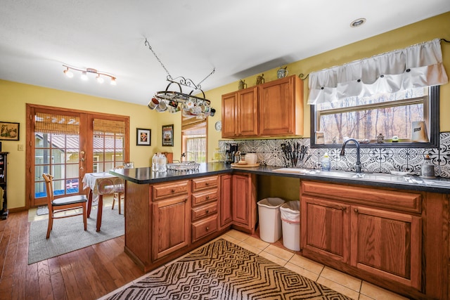 kitchen with a sink, a peninsula, brown cabinetry, decorative backsplash, and dark countertops