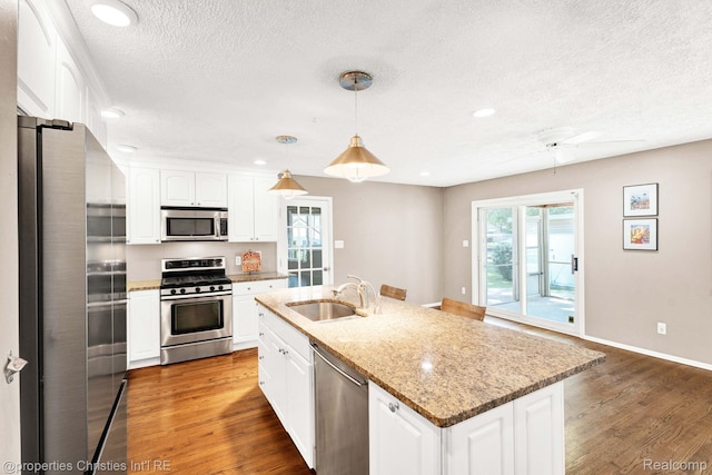 1700 Maddy Ln, Keego Harbor, MI 48320 - kitchen with stainless steel appliances, a textured ceiling, wood finished floors, white cabinetry, and light stone counters