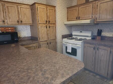 4297 N Wilderness Trl, Luther, MI 49656 - kitchen featuring white gas range oven, black microwave, under cabinet range hood, wallpapered walls, and dark countertops