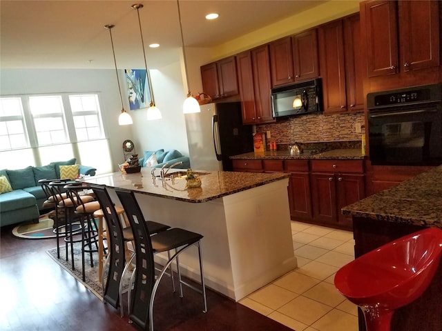 kitchen featuring black appliances, a sink, tasteful backsplash, a breakfast bar, and dark stone counters