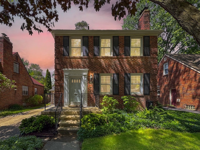 view of front of house with brick siding, central AC unit, and a chimney