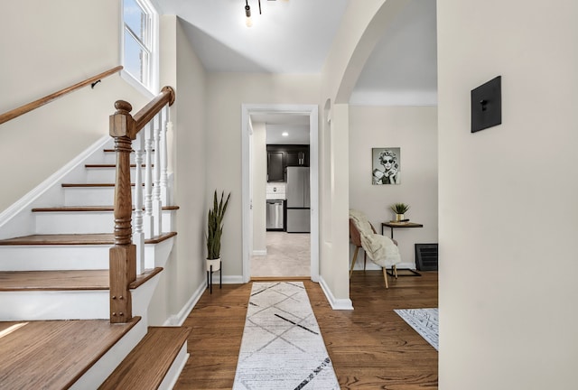entrance foyer with arched walkways, stairs, wood finished floors, and baseboards