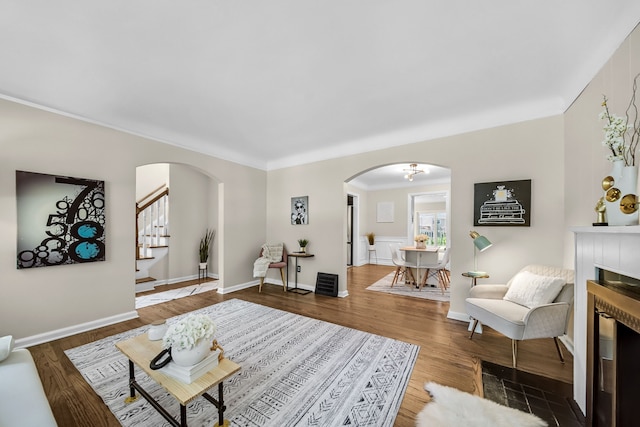 living room featuring arched walkways, wood finished floors, stairway, crown molding, and baseboards