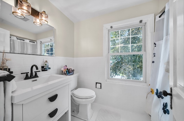 bathroom featuring tile walls, vanity, toilet, curtained shower, and wainscoting