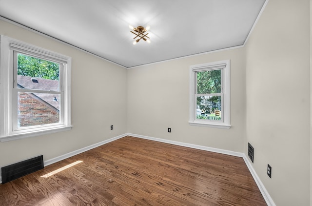 empty room with plenty of natural light, baseboards, wood finished floors, and ornamental molding