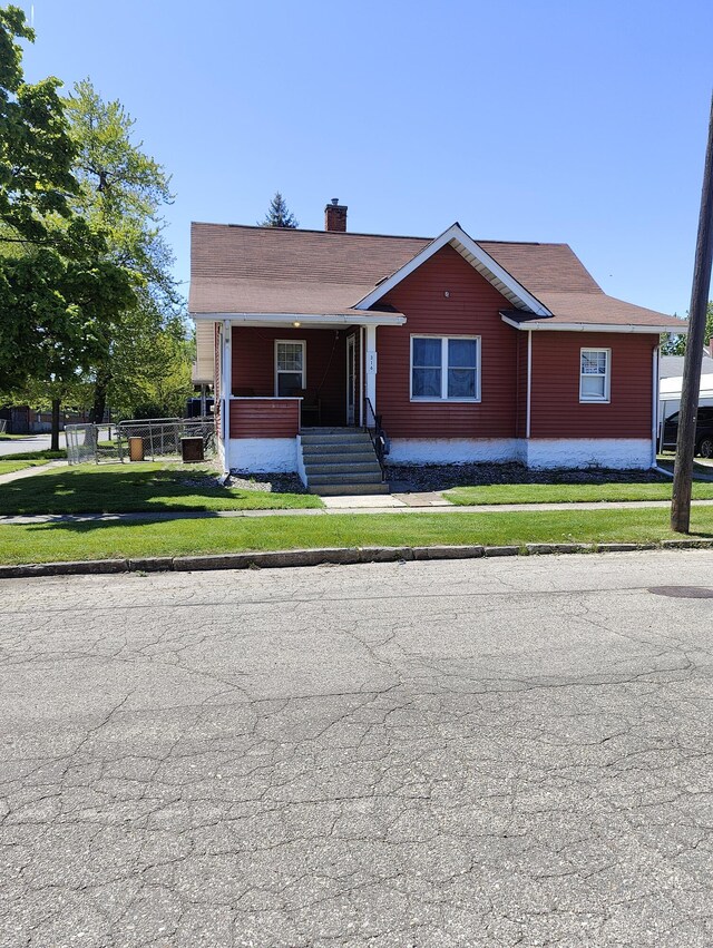 view of front of house featuring a chimney, covered porch, and a front yard