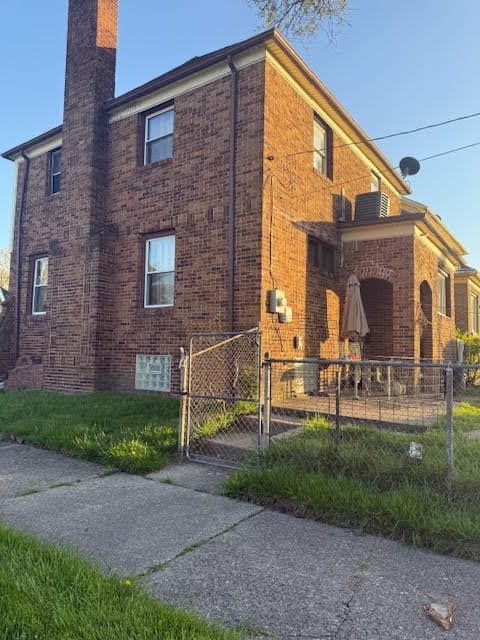 11101 College St, Detroit, MI 48205 - view of home's exterior with a chimney, brick siding, fence, and a gate