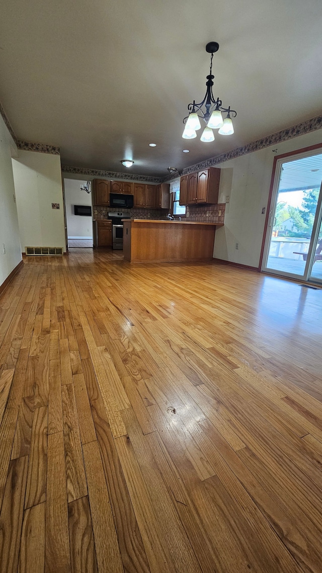 unfurnished living room with light wood-type flooring, a chandelier, and baseboards