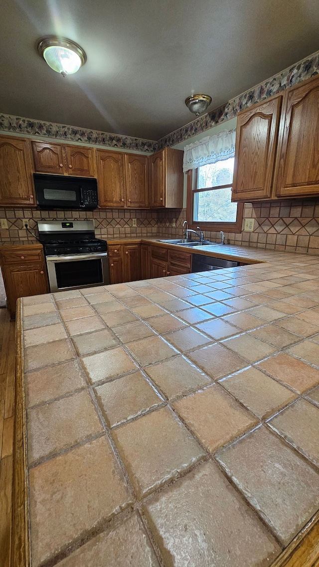 kitchen with black microwave, stainless steel gas range oven, tile countertops, and a sink