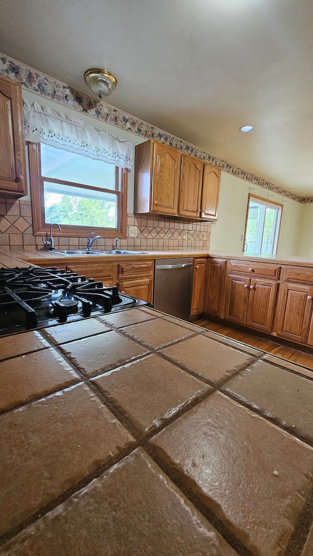 kitchen with stainless steel dishwasher, decorative backsplash, brown cabinets, and a sink