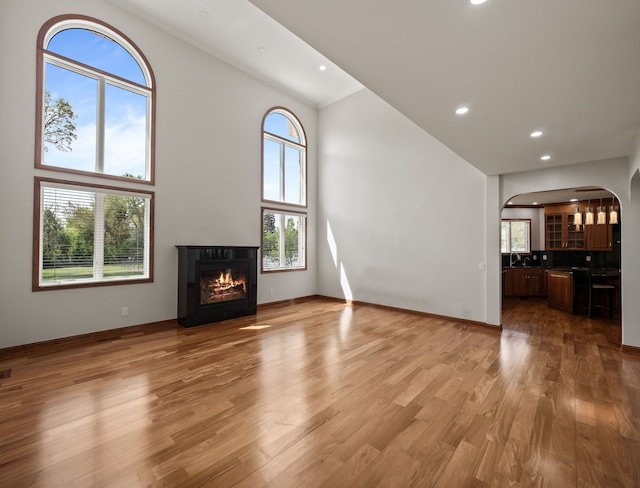 1334 Larayne Dr, Troy, MI 48085 - unfurnished living room featuring arched walkways, a glass covered fireplace, high vaulted ceiling, light wood finished floors, and recessed lighting
