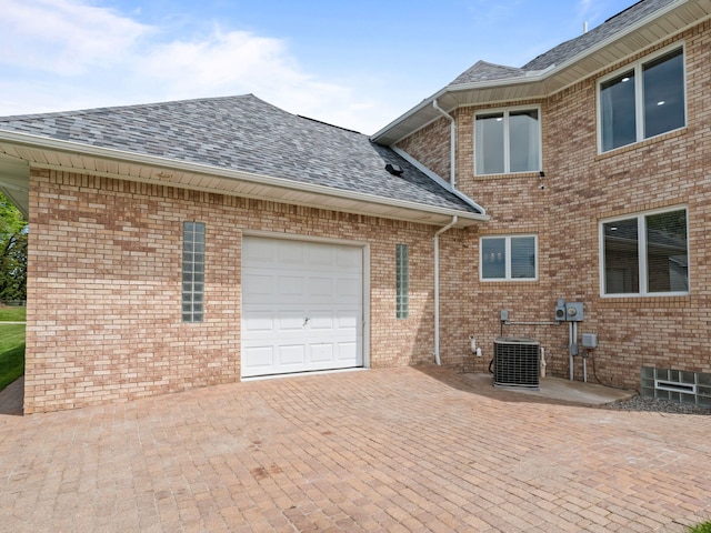 1334 Larayne Dr, Troy, MI 48085 - view of property exterior with an attached garage, a shingled roof, central AC, brick siding, and decorative driveway