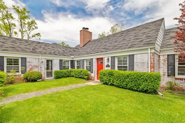 view of front of property featuring brick siding, a chimney, a front yard, and roof with shingles