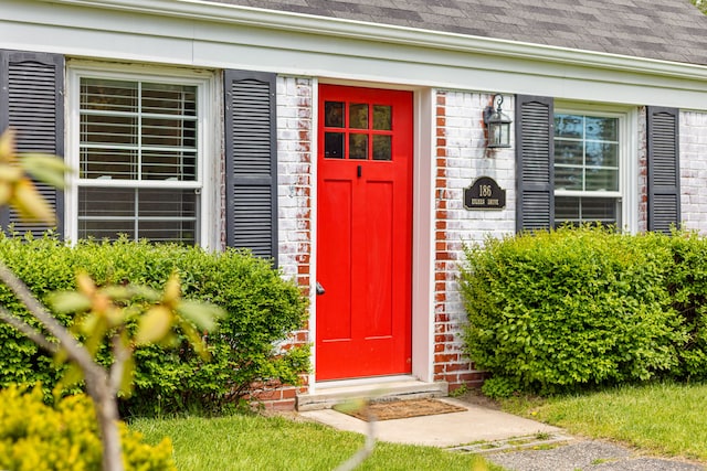property entrance with a shingled roof and brick siding