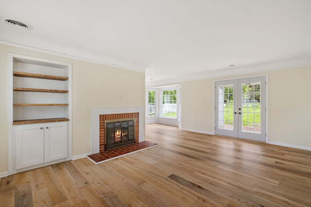 unfurnished living room with light wood-style floors, a brick fireplace, baseboards, crown molding, and french doors