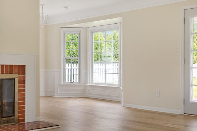 unfurnished living room with a fireplace, light wood finished floors, wainscoting, and crown molding