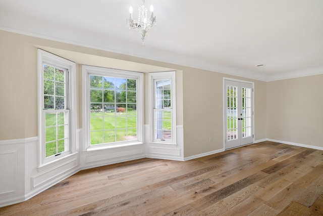 doorway featuring a chandelier, light wood-style floors, ornamental molding, and wainscoting