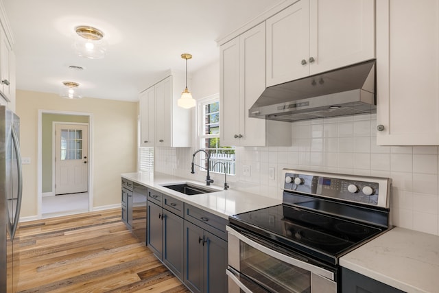 kitchen with appliances with stainless steel finishes, under cabinet range hood, a sink, light wood-style flooring, and backsplash