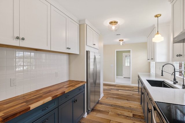 kitchen featuring butcher block counters, freestanding refrigerator, decorative backsplash, white cabinetry, and a sink