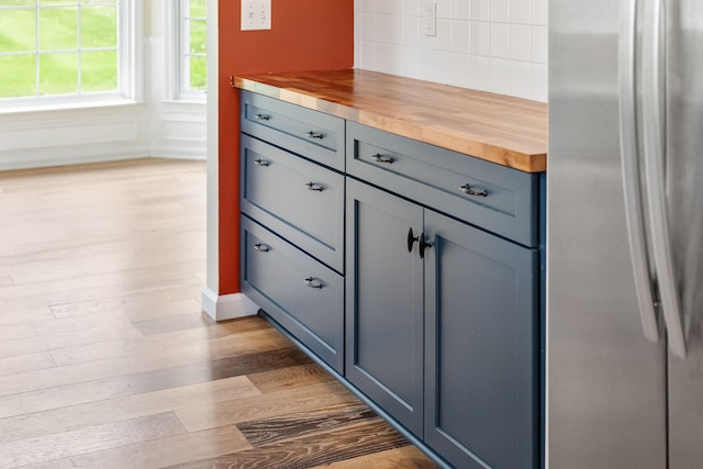 detailed view of freestanding refrigerator, wood finished floors, and decorative backsplash