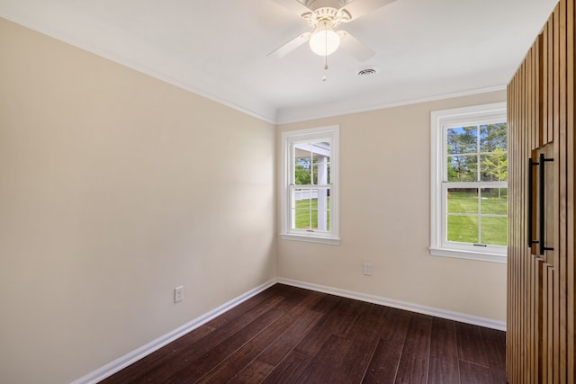 empty room with dark wood-style flooring, baseboards, healthy amount of natural light, ceiling fan, and ornamental molding