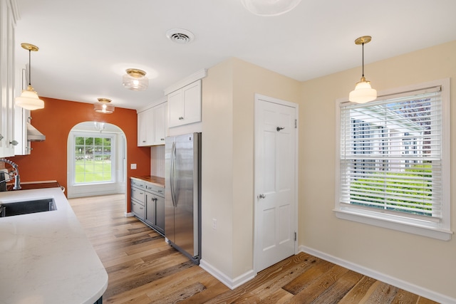 kitchen with freestanding refrigerator, light wood-type flooring, baseboards, arched walkways, and white cabinetry