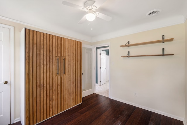unfurnished bedroom with dark wood-style flooring, baseboards, crown molding, and a ceiling fan