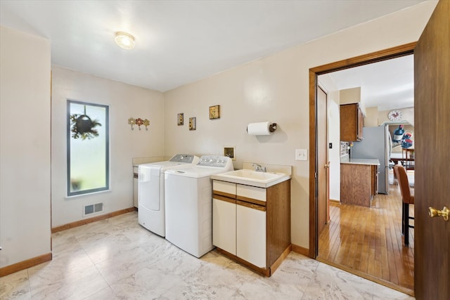 clothes washing area featuring separate washer and dryer, cabinet space, light marble finish flooring, and baseboards