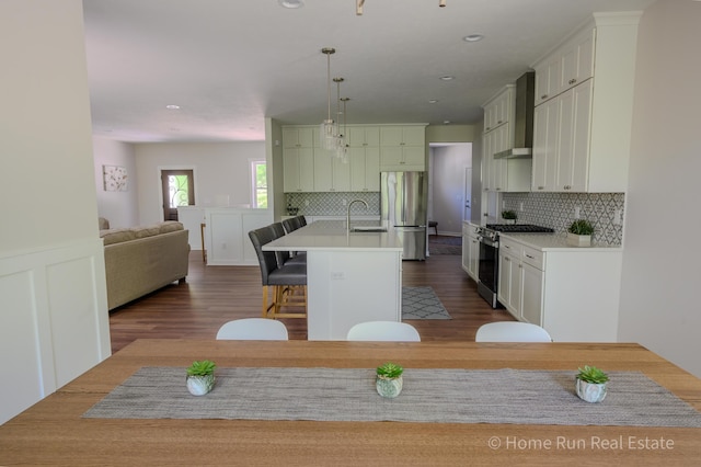 kitchen featuring stainless steel appliances, a sink, a breakfast bar area, wall chimney exhaust hood, and dark wood-type flooring