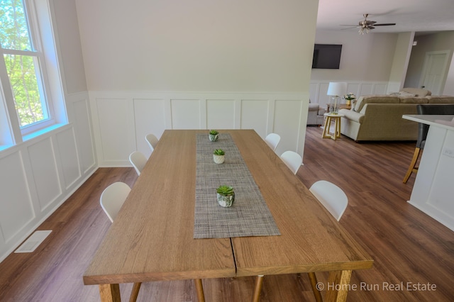 dining room featuring a decorative wall, ceiling fan, a wainscoted wall, and dark wood-style floors
