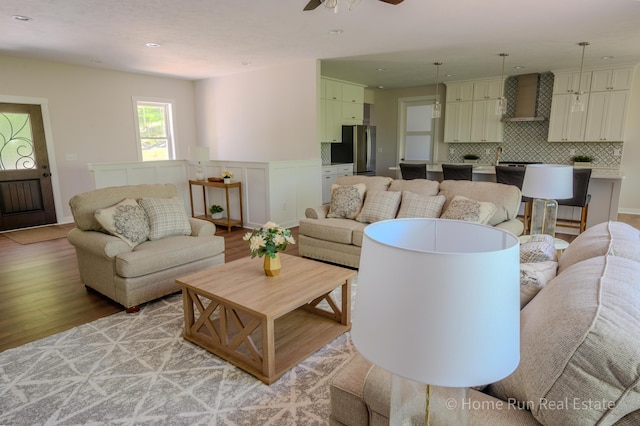 living area with light wood finished floors, ceiling fan, recessed lighting, wainscoting, and a decorative wall